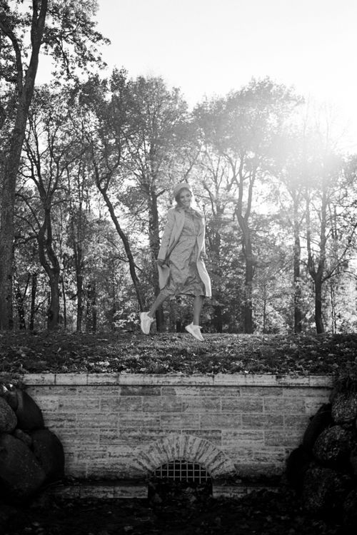 Free A woman in a coat walking on a bridge in a scenic autumn park, sunlight filtering through trees. Stock Photo