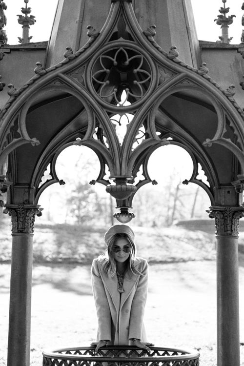 Free Black and white photo of a woman in a Gothic gazebo wearing sunglasses and a coat. Stock Photo