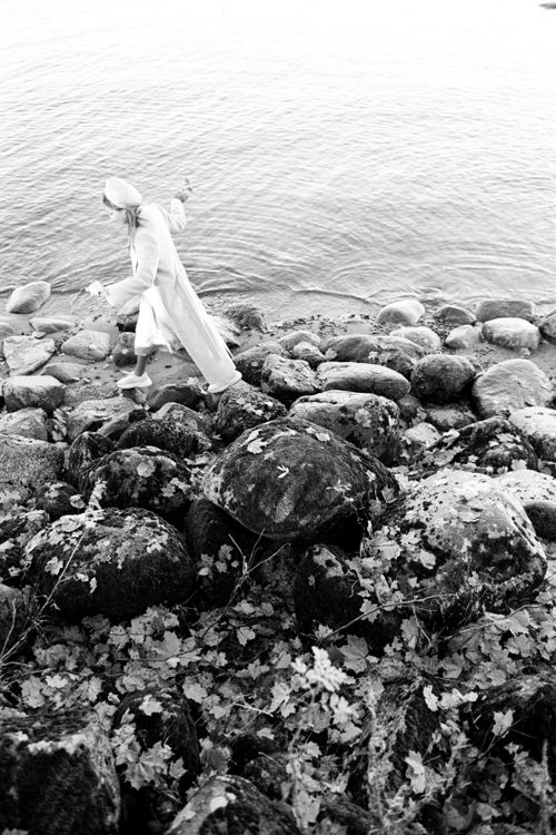 Free A woman in a white dress walks on rocky shores next to the sea in a black and white setting. Stock Photo