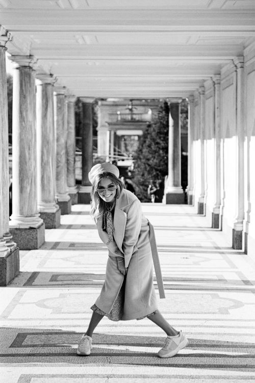 Free Woman in coat posing playfully under colonnade in a black and white setting. Stock Photo