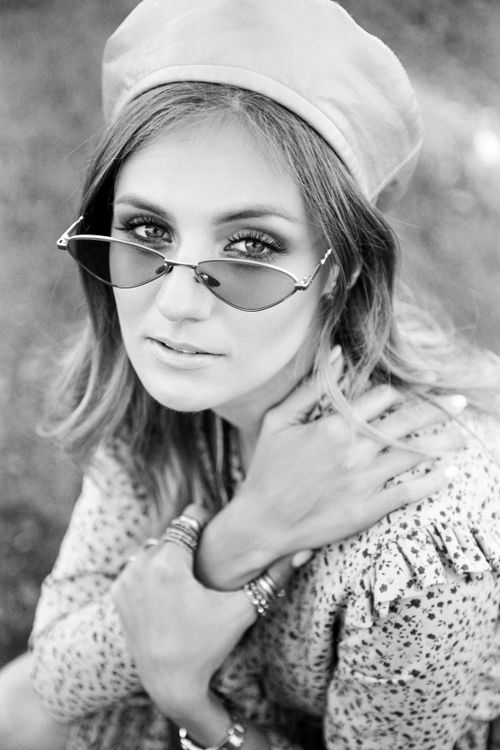 Free Black and white portrait of a young woman with sunglasses and a beret, posing outdoors. Stock Photo