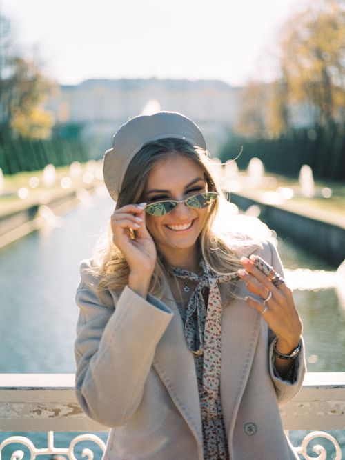 Free Charming woman in a coat and sunglasses smiles at a sunny park. Stock Photo