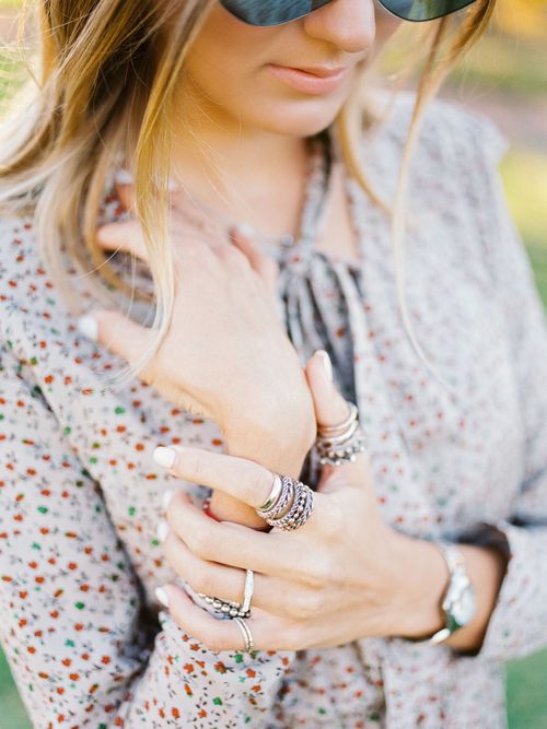 Free Close-up of a woman showcasing multiple rings and a floral dress in a sunny outdoor setting. Stock Photo