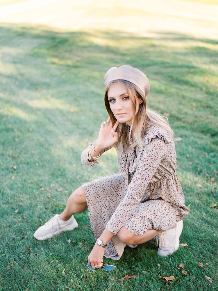 Woman In Beige Dress And Bonnet Crouching On Green Lawn