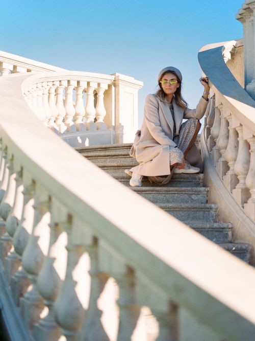 Free Stylish woman in coat and sunglasses poses on elegant outdoor staircase under clear sky. Stock Photo