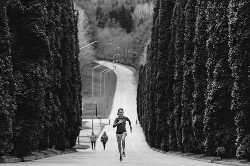 Black and White Picture of a Woman Running along an Alley Lined with Trees