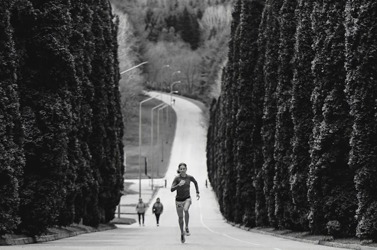 Black And White Picture Of A Woman Running Along An Alley Lined With Trees