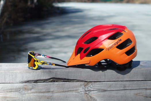 Close-up of a colorful bicycle helmet and sunglasses on a wooden railing outdoors.