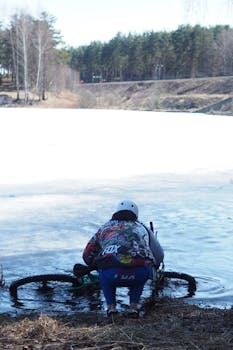 Cyclist in sportswear retrieving bike from icy lake in winter scenery