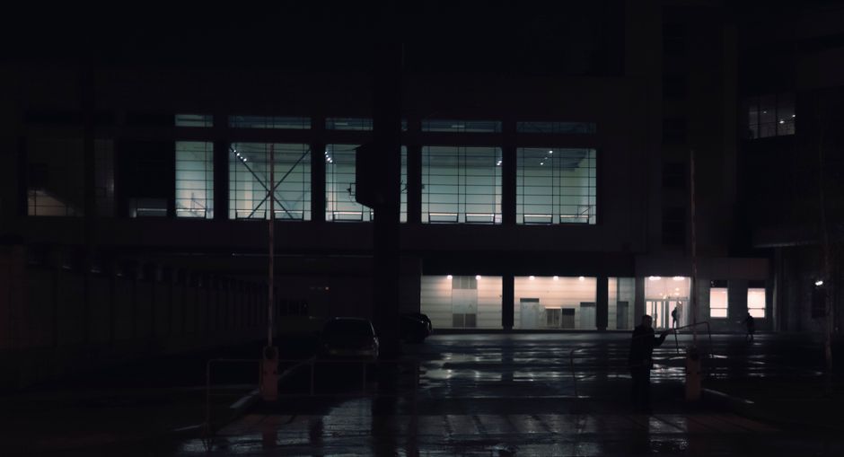 Night view of a modern building with illuminated windows and reflective wet surface.