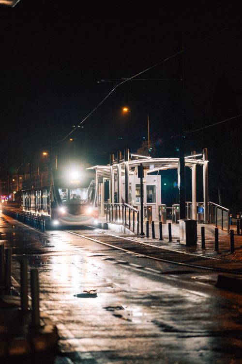 Free Illuminated tram arriving at a city station at night with wet streets. Stock Photo