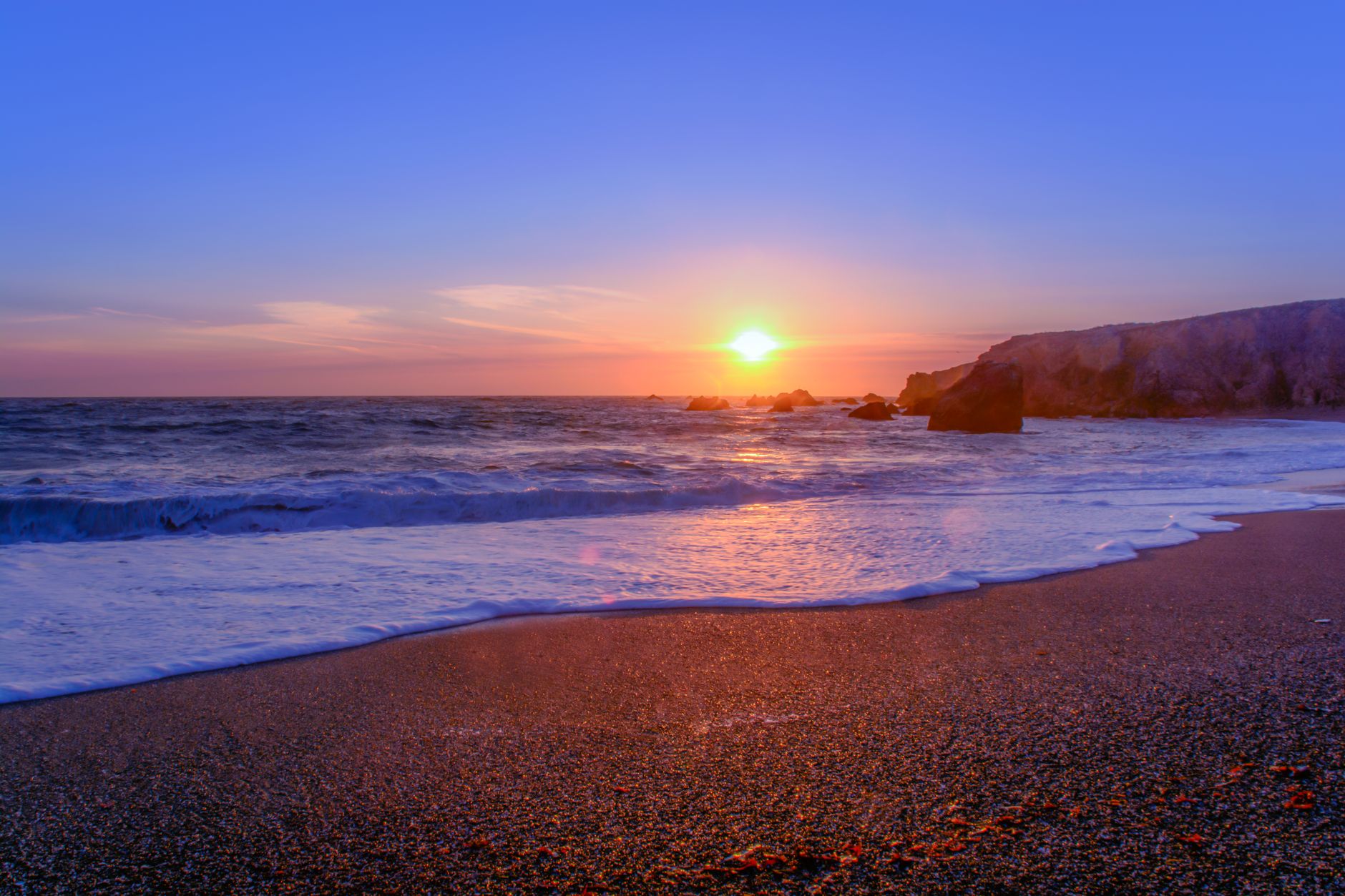 Beautiful sunset over Bodega Bay beach with waves and rock formations.