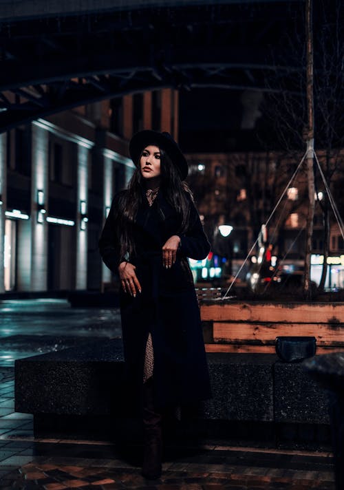 A Woman in Black Coat Standing on the Street at Night