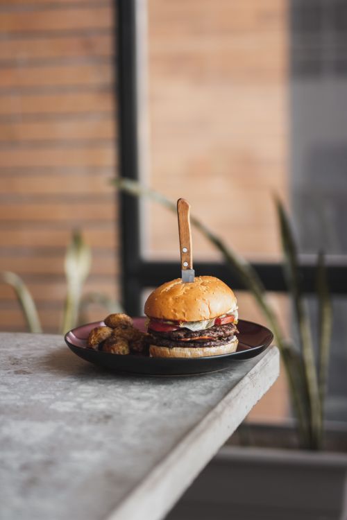 Free A gourmet burger paired with roasted potatoes on a black plate, knife inserted, on a kitchen counter. Stock Photo