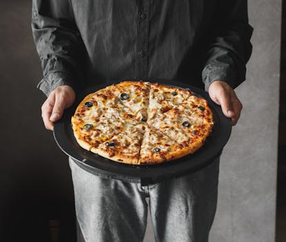 Appetizing pizza with cheese and olives on a tray, held by a person.