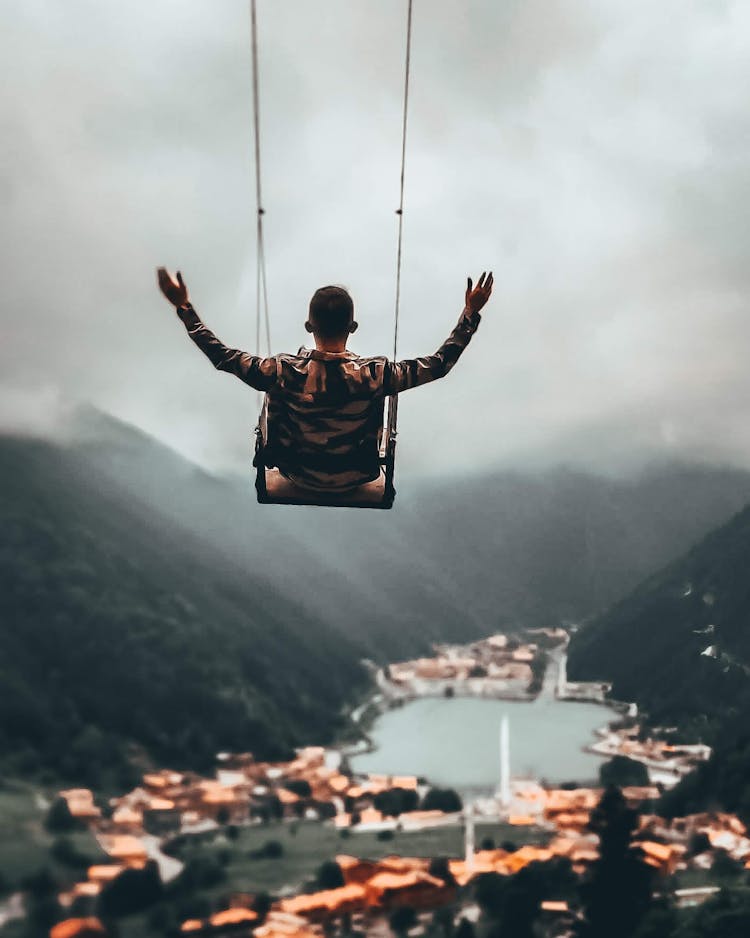 Man Swinging Above City, Lake And Mountains