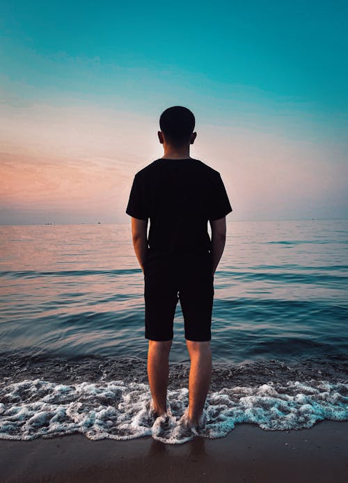 Free Man Standing on Beach During Sunset Stock Photo