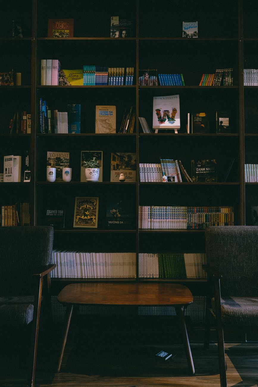 A warm and inviting library room featuring bookshelves, armchairs, and a wooden table.