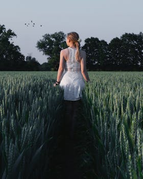 日落时分，一位穿着白色连衣裙的金发女子在德国一片宁静的麦田里散步