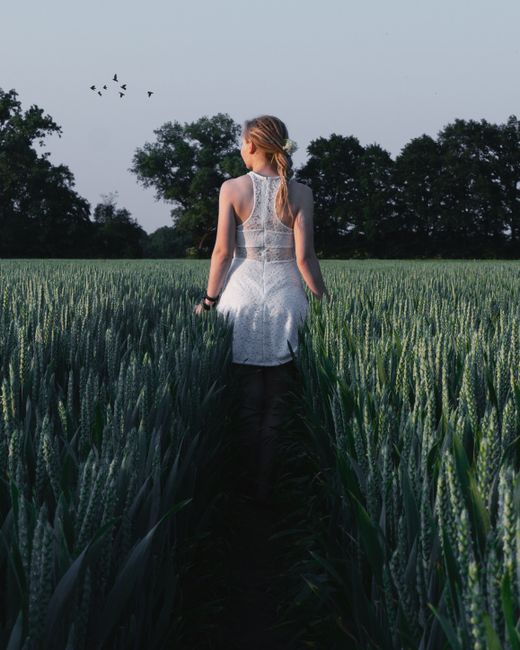 Blonde woman in white dress walking in a peaceful wheat field at sunset in Germany.