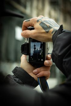 Tattooed hands holding a camera capturing a building silhouette on screen.
