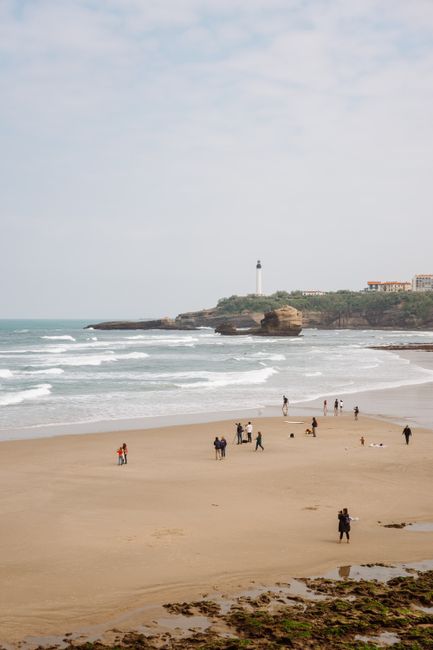 Tranquil sandy beach in Biarritz, France with distant lighthouse and calm ocean waves.