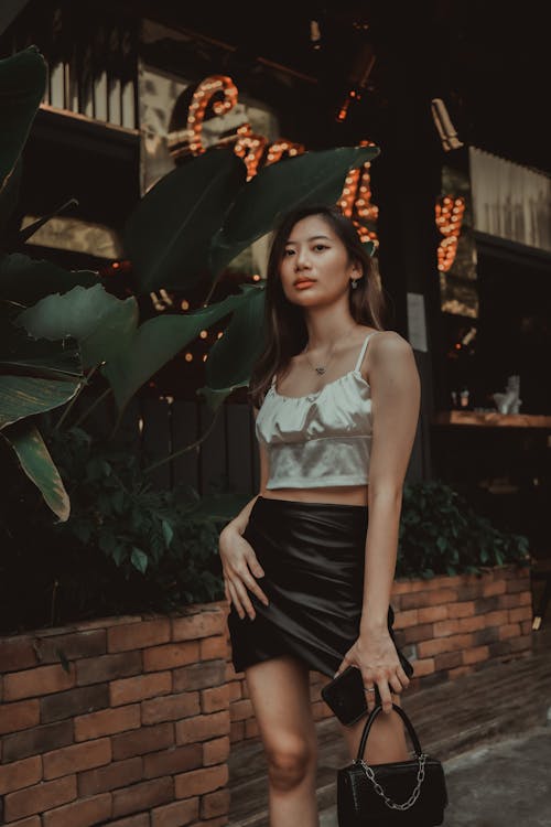 Woman in White Crop Top and Black Skirt Standing Beside Green Plants