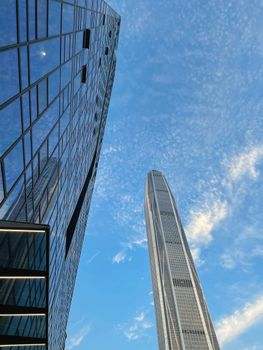 Low angle view of futuristic skyscrapers with glass panels against a vibrant blue sky.