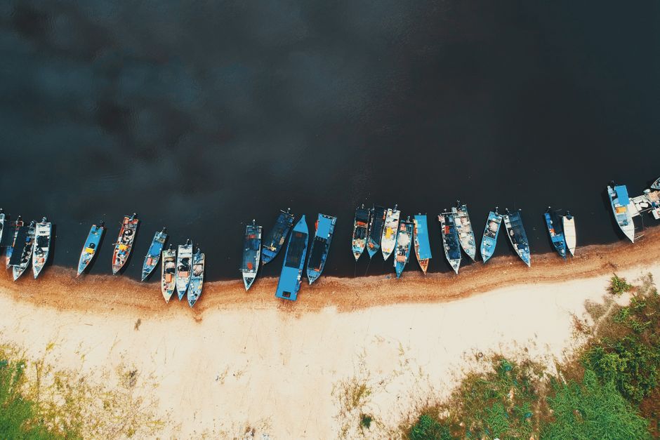 Aerial view of colorful boats moored along a sandy shore against a dark water backdrop.