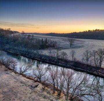 A scenic winter landscape featuring a river and bare trees at sunset in Minnesota, USA.