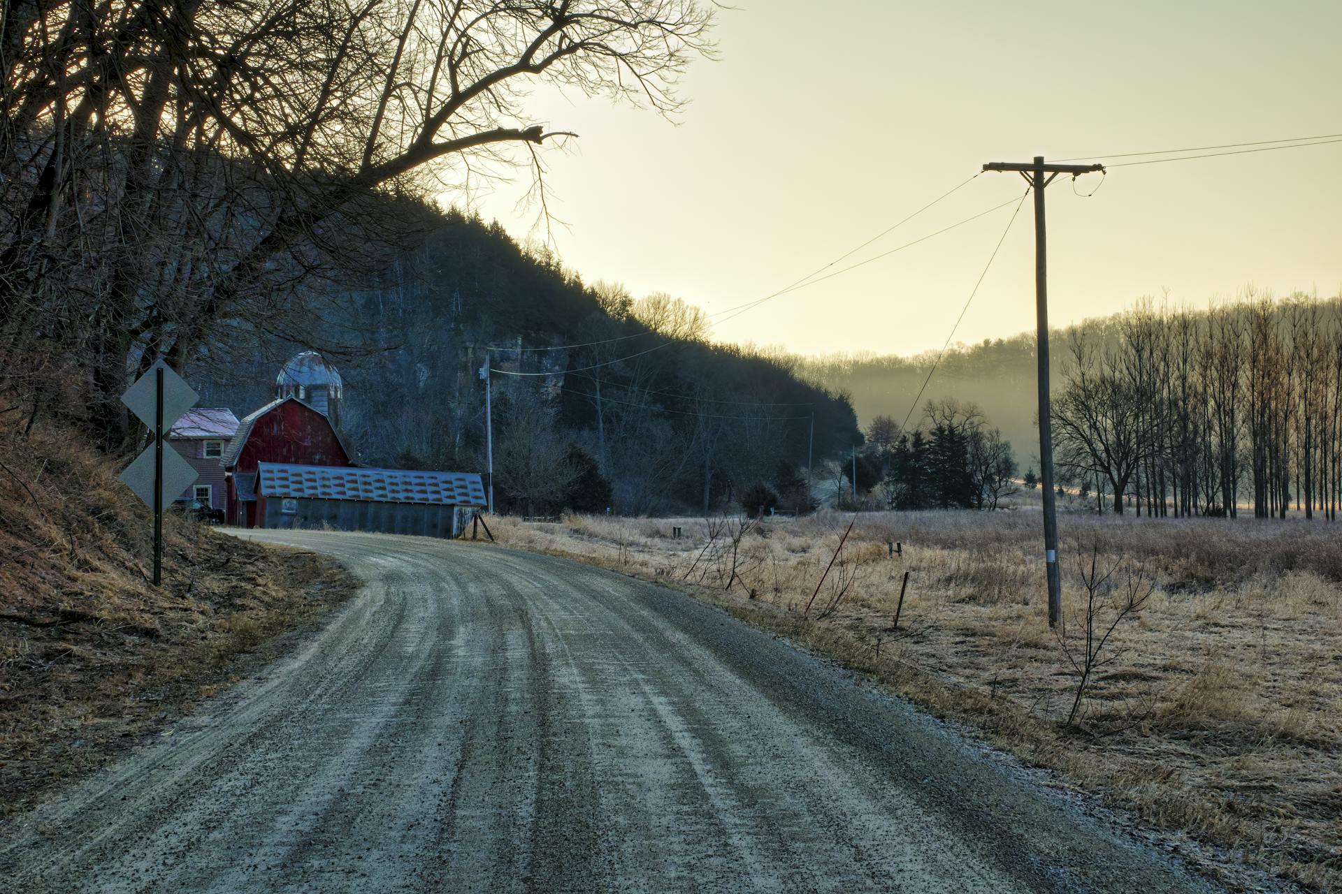 Peaceful rural road in Minnesota during fall, featuring a classic red barn and barren trees.