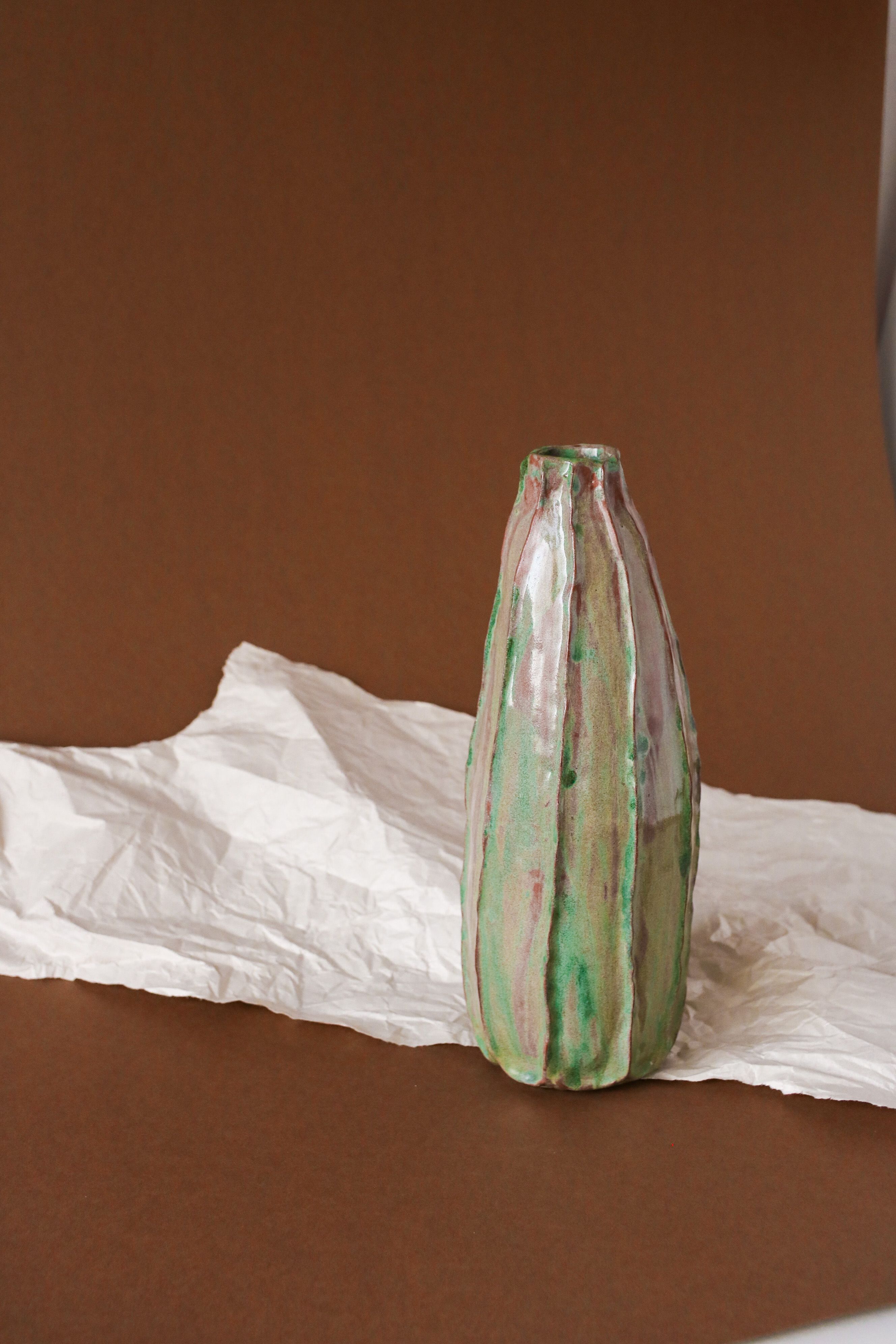 A green-glazed ceramic vase on crumpled paper against a brown backdrop — photo by Andreea Ch on Pexels