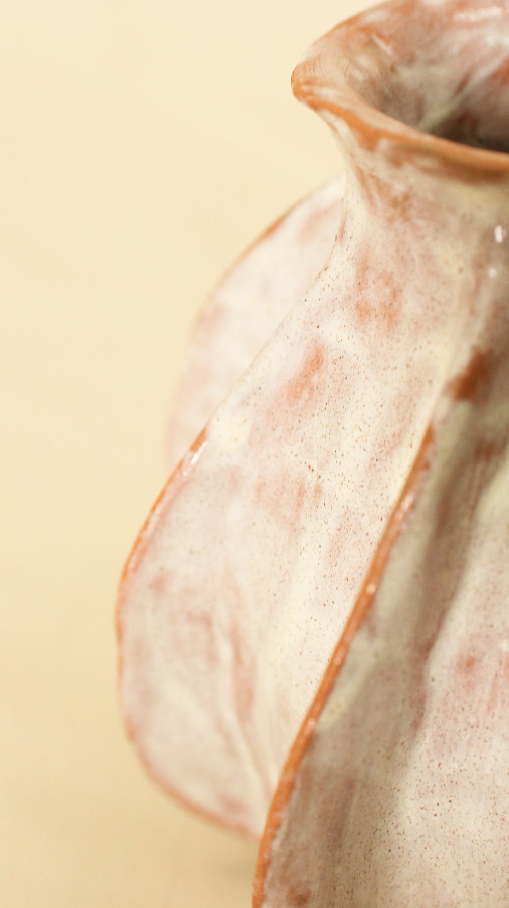 Close-up of a pale glaze breaking over the textured rim of a vase
