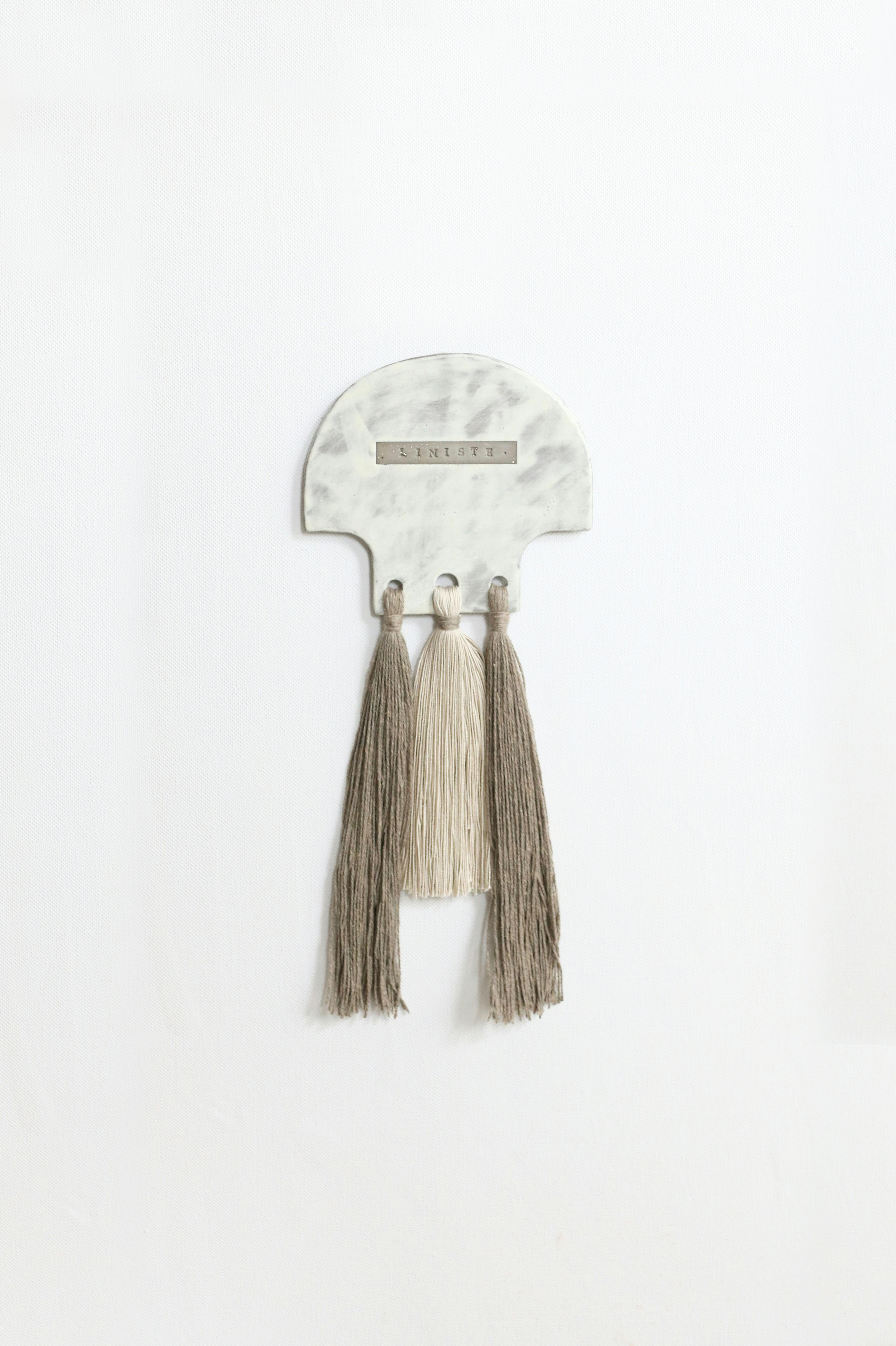 Elegant decorative wall hanging with tassels on a marble-like plaque.
