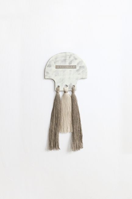 Elegant decorative wall hanging with tassels on a marble-like plaque.