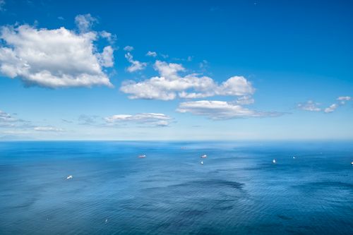 Free A tranquil aerial view of the vast ocean under a clear blue sky with scattered clouds. Stock Photo