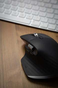 Close-up of a sleek black wireless mouse on a wooden desk beside a keyboard.