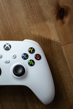Close-up of a white gaming controller on a wooden surface, showcasing colorful buttons.