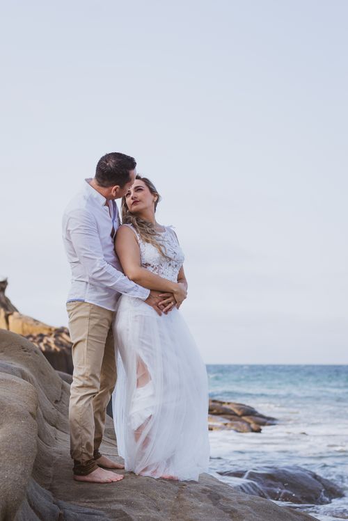 Free A couple embracing by the seaside, enjoying a romantic moment on the rocks at sunset. Stock Photo