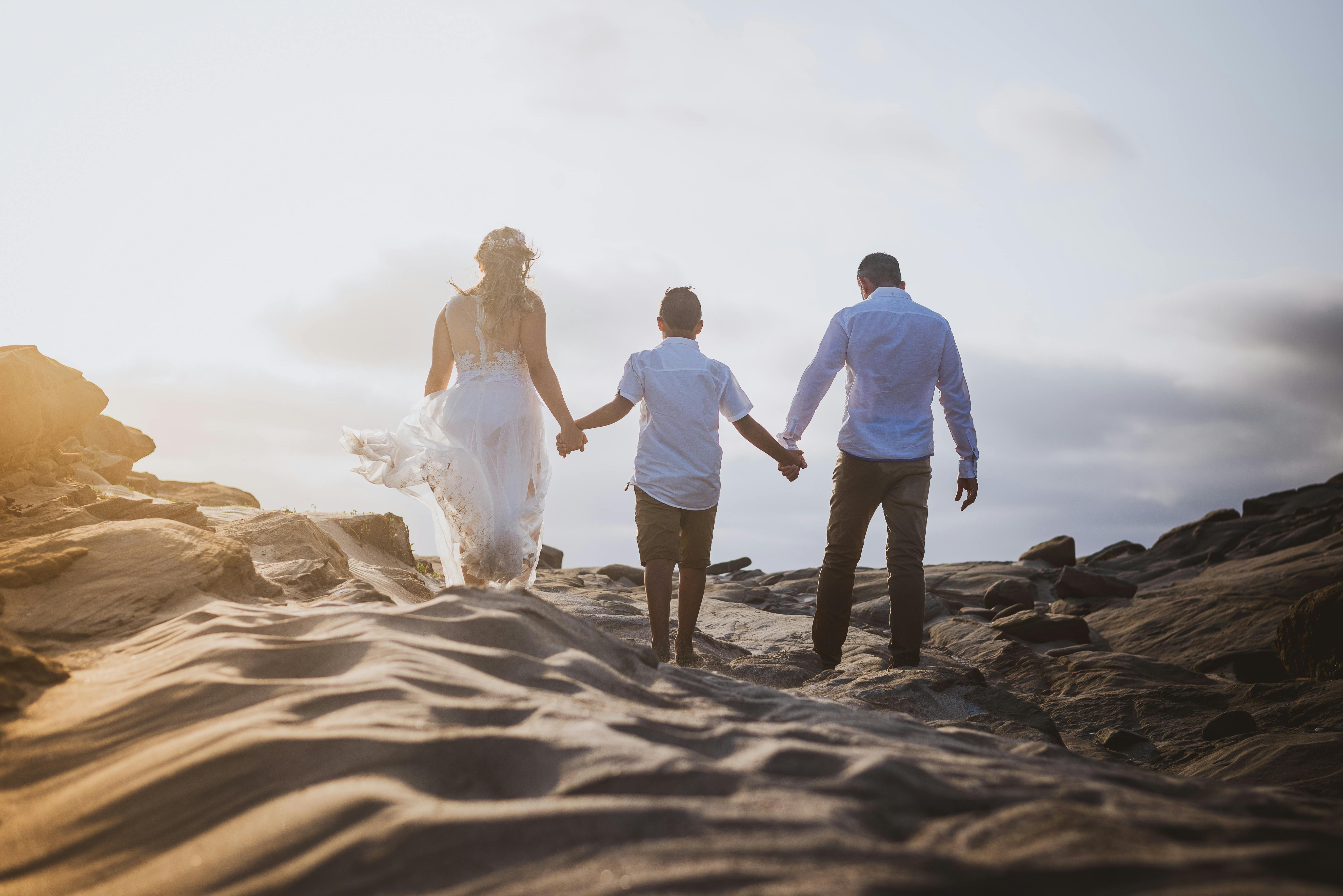 A family holding hands while walking on a sandy beach path with the sun setting in the background.