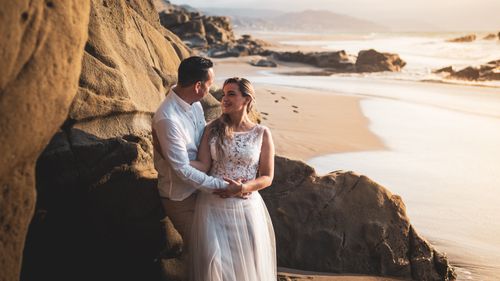 Free A romantic couple embracing on a scenic beach during sunset, expressing love and affection. Stock Photo