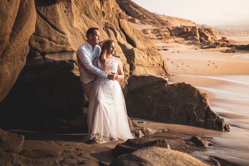 Free A couple embraces on a rocky seaside during sunset, evoking romance and serenity. Stock Photo