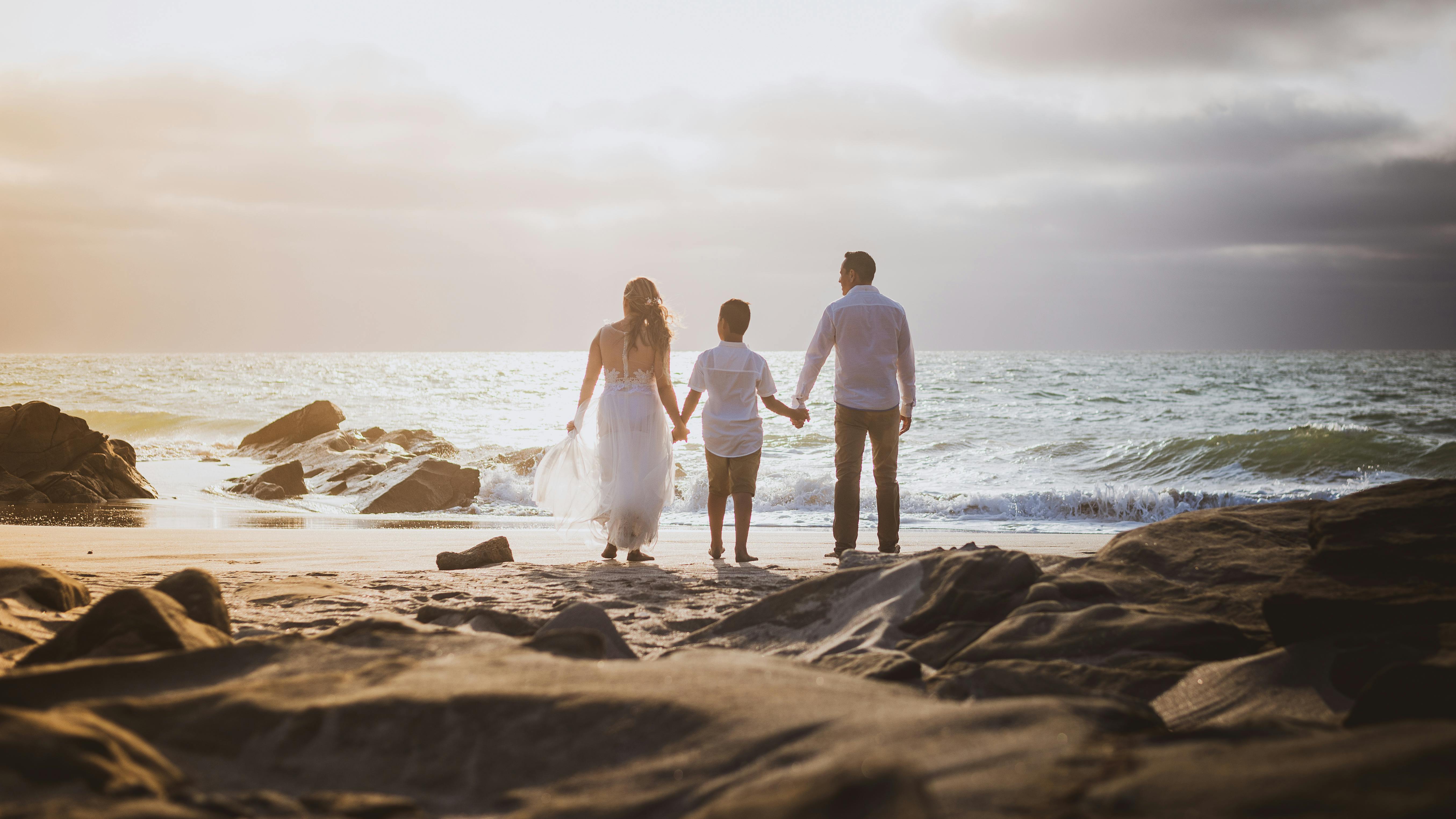 A family stands together on the beach at sunset, holding hands and enjoying the ocean view.