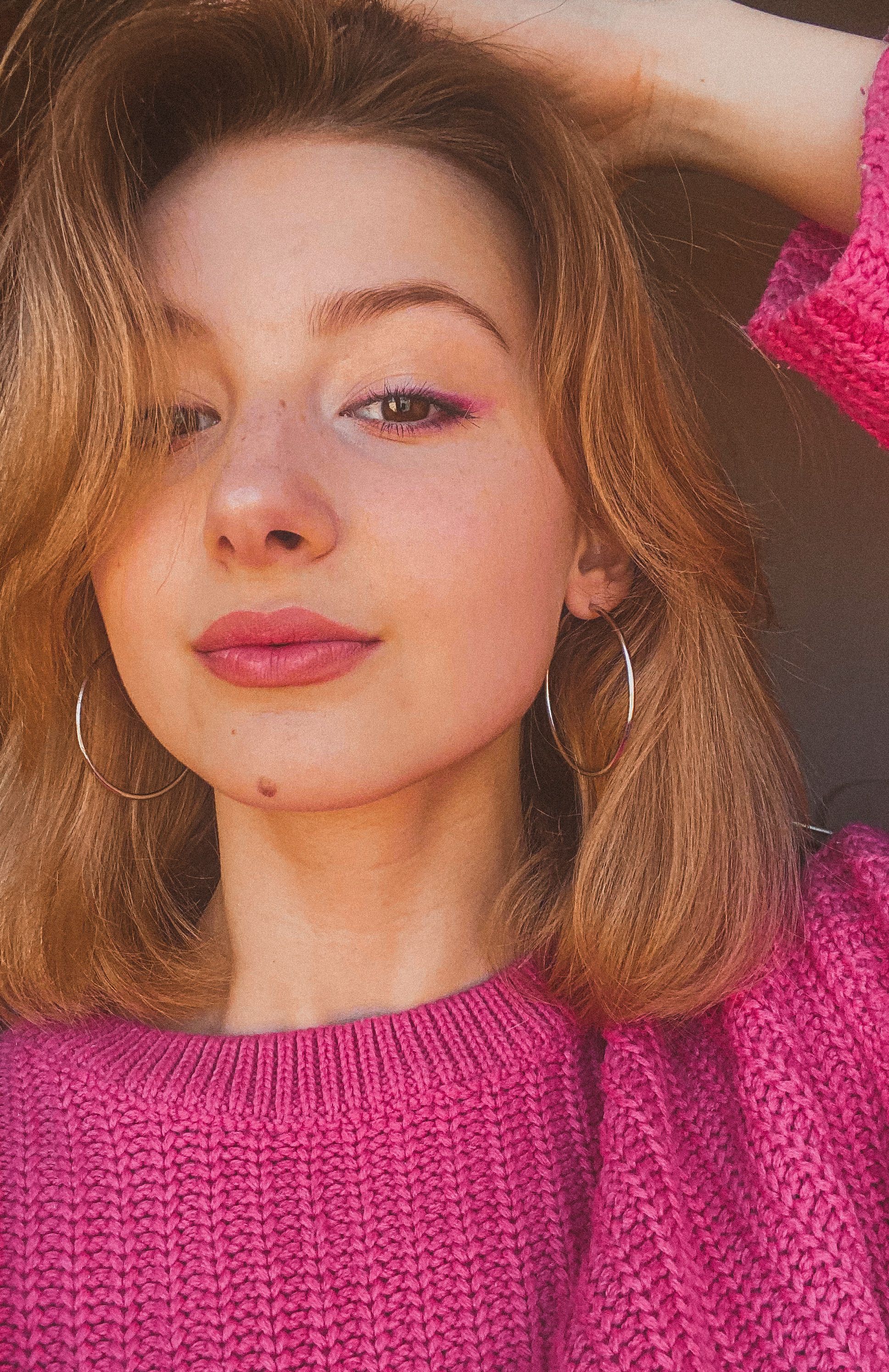 Close-up portrait of a young woman wearing a pink sweater with natural light.