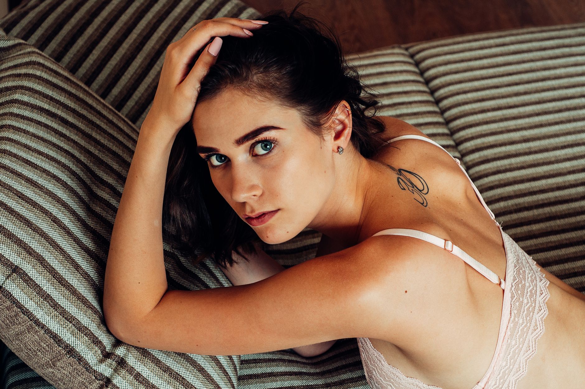 Elegant woman in lingerie posing indoors, showcasing beauty and style with a visible tattoo.