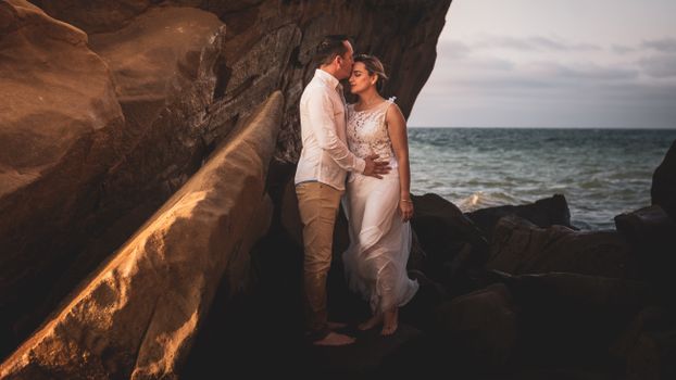 A couple sharing a tender moment by the rocky seashore at sunset.