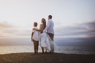 Backs of Newlyweds Standing on a Beach with their Son