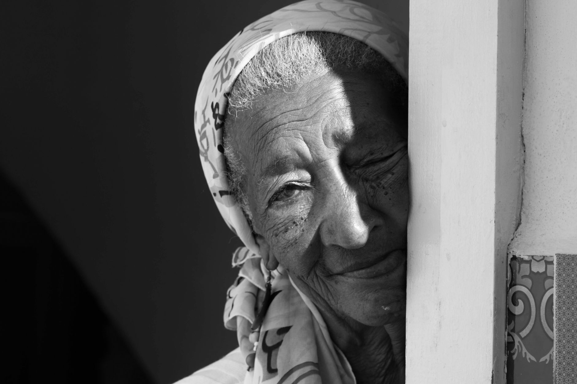 Monochrome close-up portrait of an elderly woman with a headscarf, showcasing wisdom and emotion.