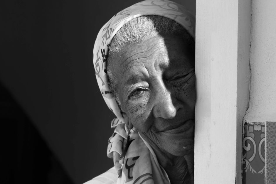 Monochrome close-up portrait of an elderly woman with a headscarf, showcasing wisdom and emotion.