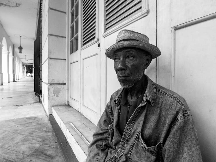 Old Man In Straw Hat Sitting At Door Under Colonnade